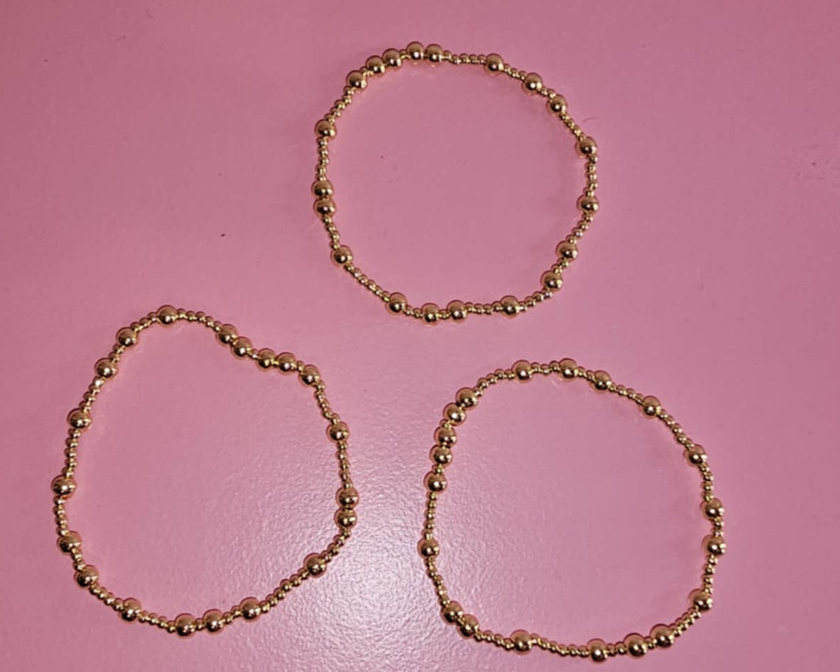 Three gold bracelets on a pink background