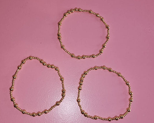 Three gold bracelets on a pink background